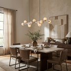The brushed-nickel Clérachic chandelier glows over a dining table with olive branches and linen curtains.