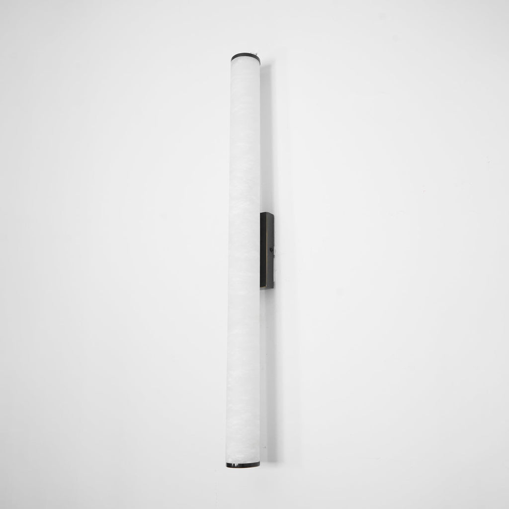 Slim alabaster wall sconce with brass finish against pale wall