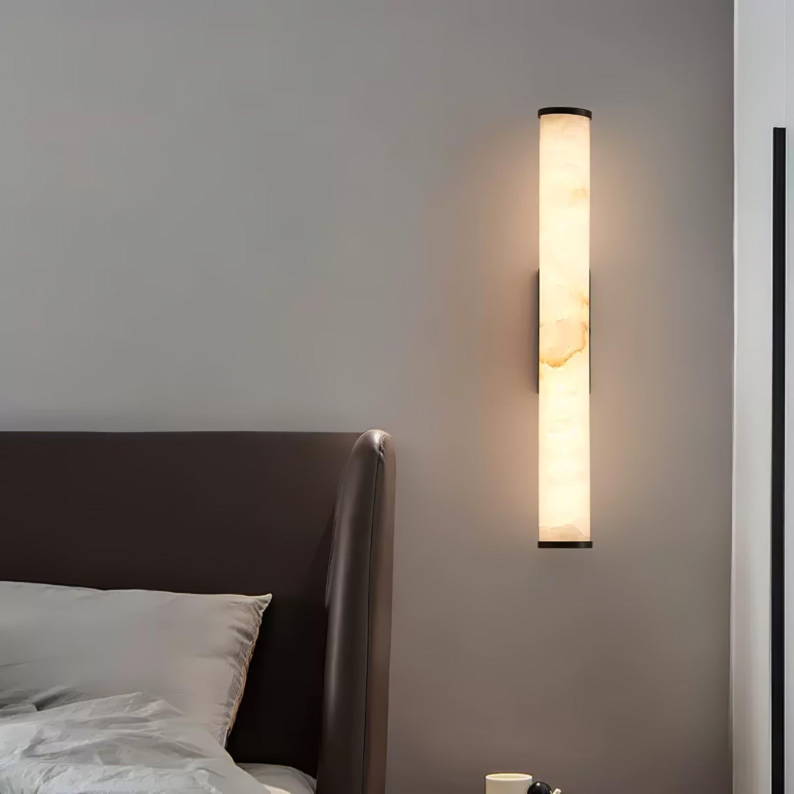 Tall black wall sconce with translucent alabaster shade lit warmly