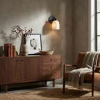 This Clérachic wall sconce in black finish lights a wall above a walnut sideboard and a grey armchair.