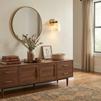 This Clérachic wall sconce in brass finish hangs beside a round mirror above a walnut sideboard with vases.