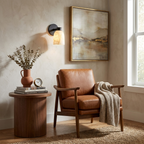 Beside a framed landscape painting, this Clérachic wall sconce in black finish lights a leather armchair below.