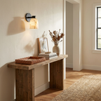 In a hallway, this Clérachic wall sconce in black finish lights a reclaimed-wood console table below.