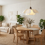 A rattan-and-linen living space gathers beneath this glowing Clérachic pendant above a round wood table.