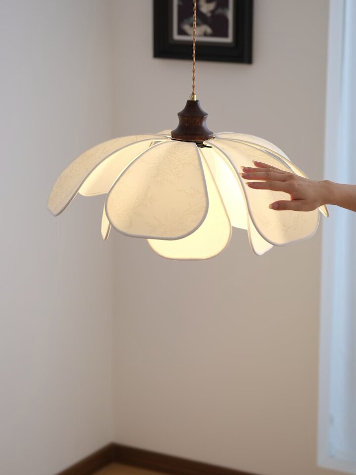 A hand reaches toward the fabric petals of this lit Clérachic pendant in close-up.
