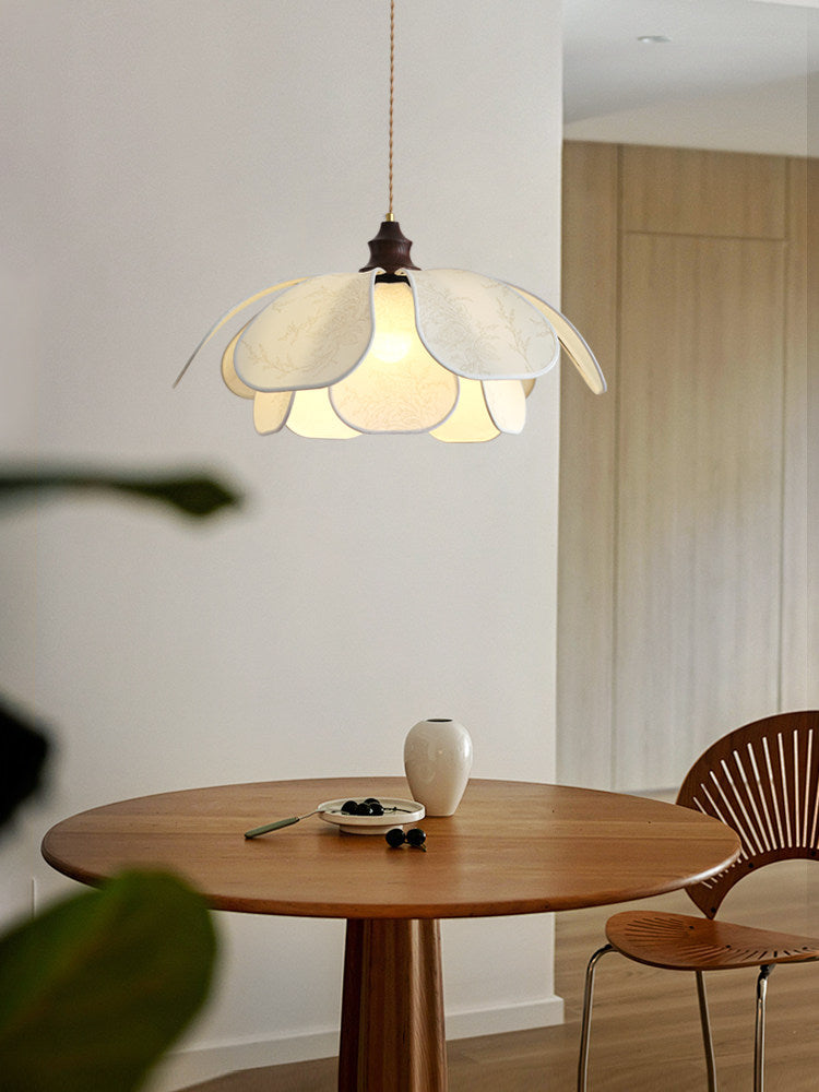 This Clérachic pendant lights a round wood table set with a ceramic bowl beside a woven cane chair.