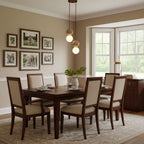 A two-tier Clérachic pendant hangs in front of a bay window in a beige dining room hung with framed photos.