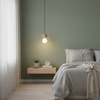 A single Clérachic pendant glows against a sage-green wall above a floating nightstand and a small plant.