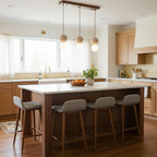 A linear Clérachic fixture lights an oak kitchen island with grey upholstered stools.