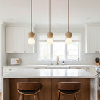 Three Clérachic pendants hang above a white kitchen island with wood-backed chairs.