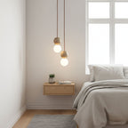 A cluster of Clérachic pendants lights a bedroom corner above a floating oak nightstand and a small potted plant.