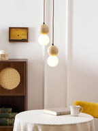 A two-tier Clérachic pendant hangs beside a rattan-fronted cabinet holding books and a small framed artwork.