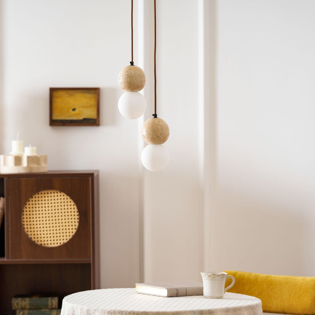 A two-tier Clérachic pendant hangs above a round table set with a book and a cup, near a rattan cabinet.