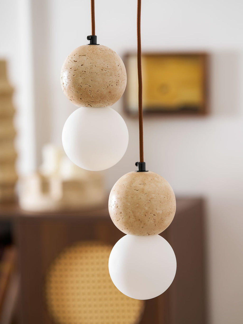 Pitted stone texture shows on this Clérachic pendant's travertine sphere, set above its opal glass globe near a rattan cabinet.