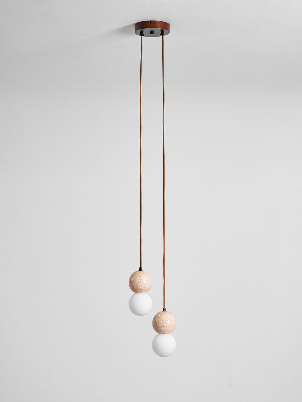 A two-light Clérachic pendant's round canopy drops two cords ending in small travertine and glass spheres, studio shot.