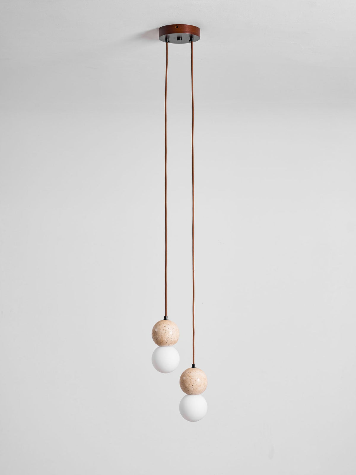 A two-light Clérachic pendant's round canopy drops two cords ending in small travertine and glass spheres, studio shot.