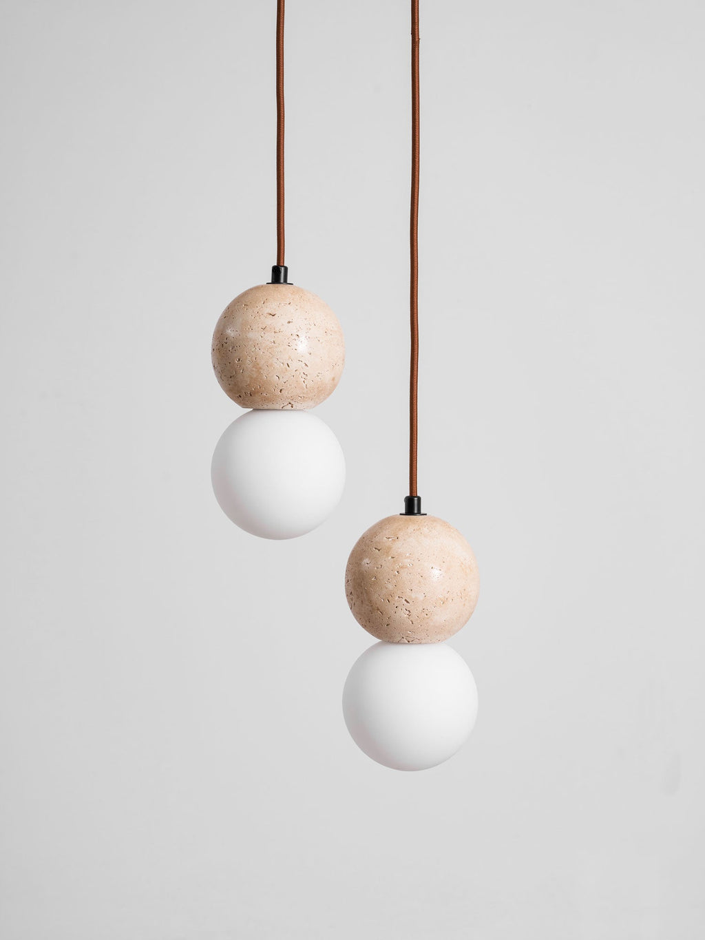 Soft light rises from the opal glass globe beneath this Clérachic pendant's travertine sphere, on a plain grey backdrop.