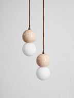 Soft light rises from the opal glass globe beneath this Clérachic pendant's travertine sphere, on a plain grey backdrop.