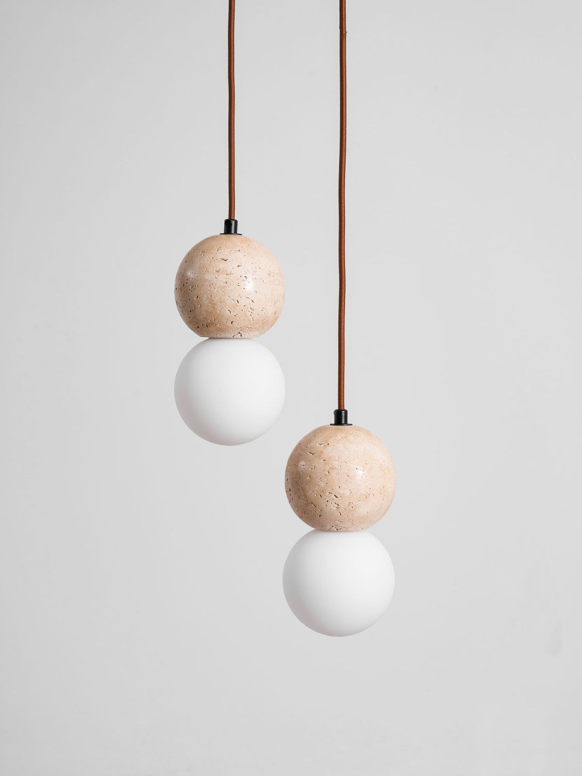 Soft light rises from the opal glass globe beneath this Clérachic pendant's travertine sphere, on a plain grey backdrop.