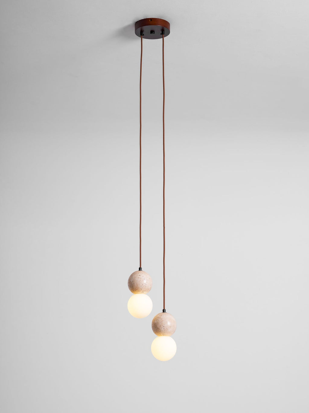 Two short cords drop small travertine and glass spheres from this Clérachic pendant's round canopy, studio shot on grey.