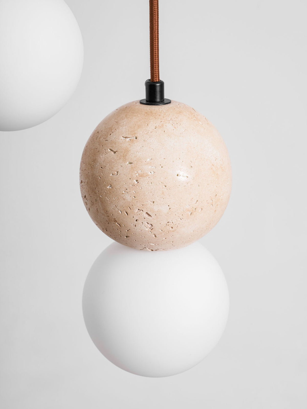 A travertine sphere sits above an opal glass globe on this Clérachic pendant, a second globe visible at the frame's edge.