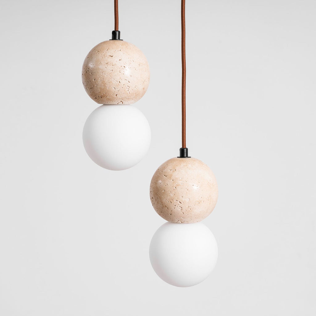Two Clérachic pendants of different drop lengths show travertine spheres paired with opal glass globes.