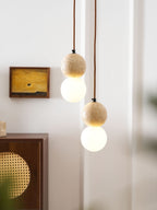 A travertine sphere and opal glass globe hang close together on this Clérachic pendant, rattan cabinet blurred behind.
