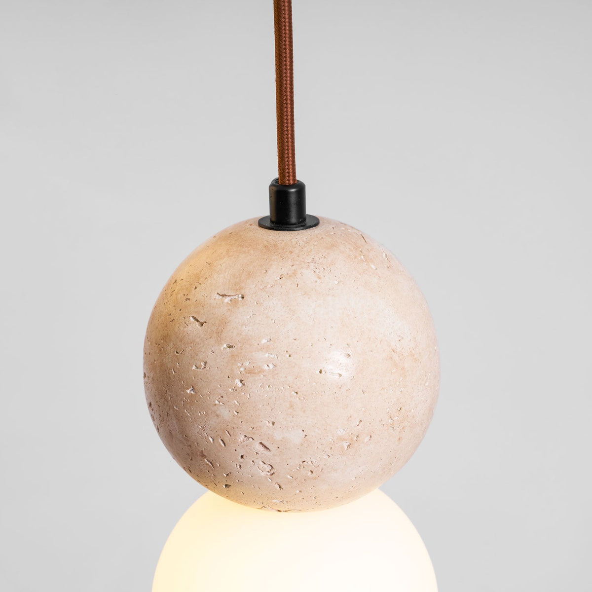 Pitted stone texture fills the frame on this Clérachic pendant's travertine sphere, its glass globe glowing just beneath.