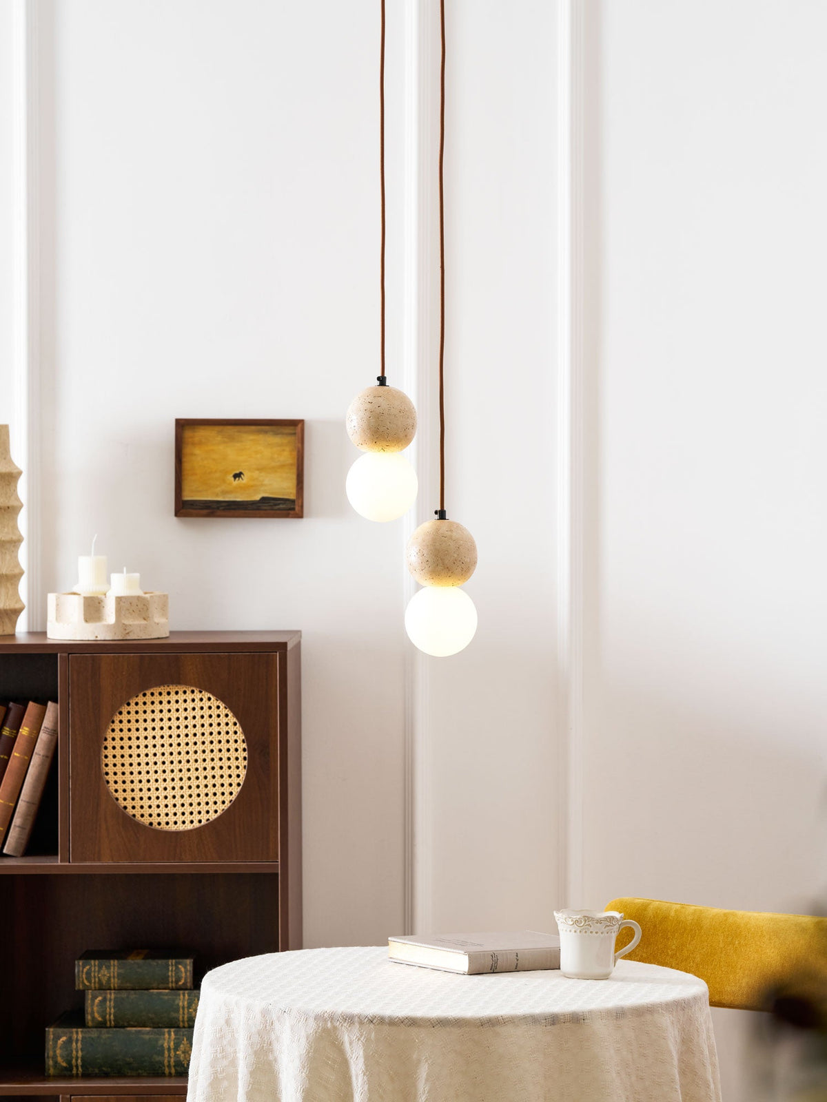 A single Clérachic pendant hangs near a rattan-fronted cabinet set with candle holders and stacked books.