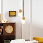 A three-tier Clérachic pendant cluster hangs beside a rattan-fronted cabinet near a small framed artwork.