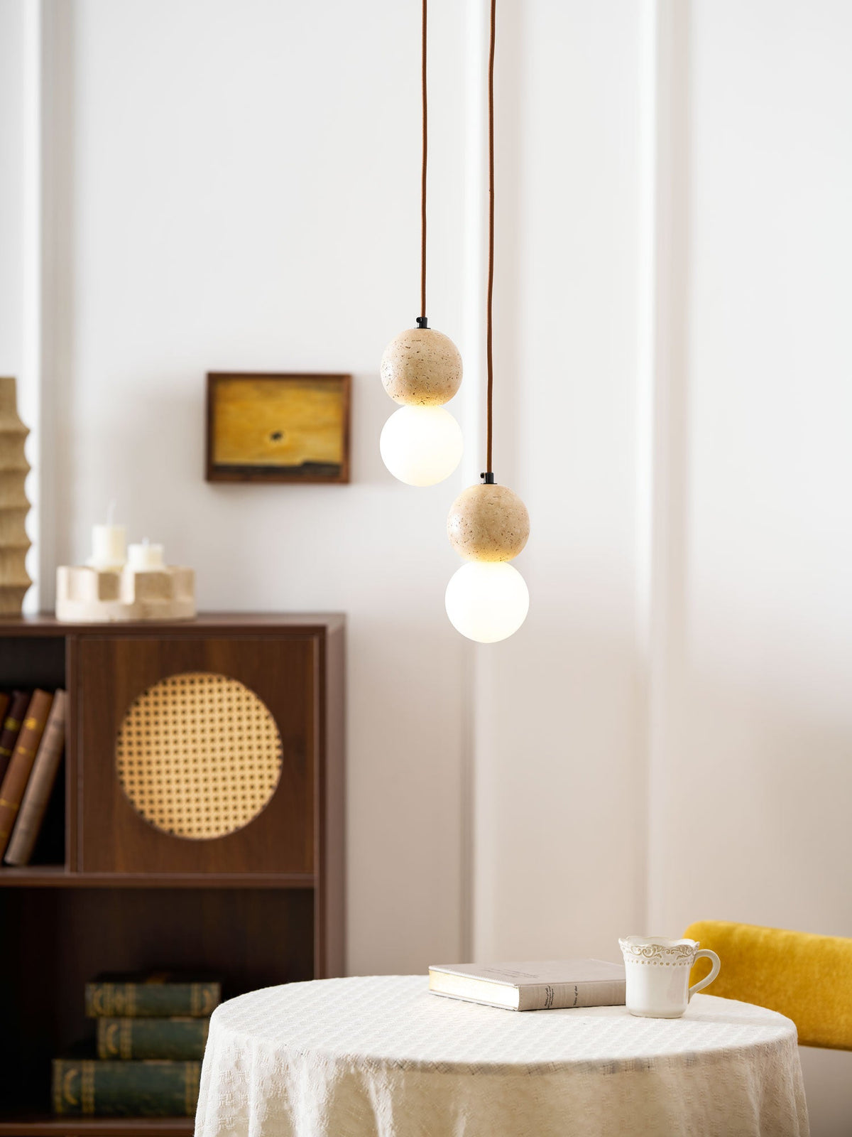 A two-tier Clérachic pendant hangs above a round table holding a cup and a stack of books.