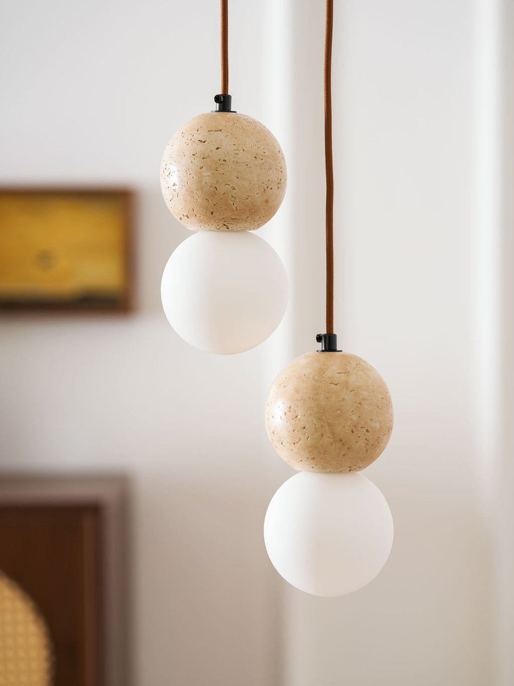 Fine mineral flecks mark the travertine sphere on this Clérachic pendant, paired with an opal glass globe below.