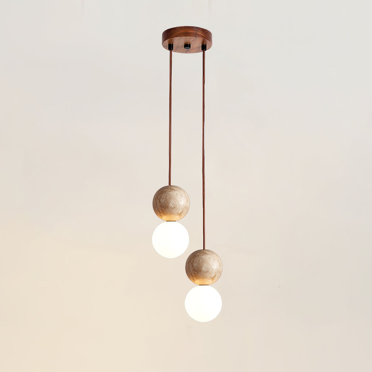 Two cords of differing length drop travertine and glass spheres from this Clérachic pendant's round canopy, studio shot.