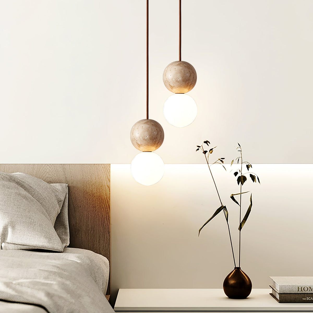 A two-tier Clérachic pendant lights a bedside table with a dark vase and a sprig of dried leaves.