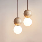 Warm light catches the travertine sphere of this Clérachic pendant, seen close above its opal glass globe.