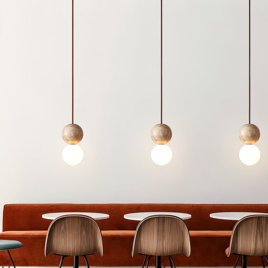 Three Clérachic pendants hang low over a rust velvet banquette with wood dining chairs.