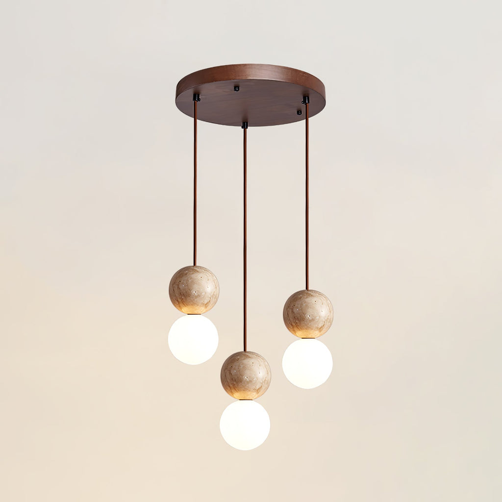 A three-light Clérachic pendant's round canopy drops staggered travertine and glass spheres, studio shot on white.