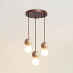 A three-light Clérachic pendant's round canopy drops staggered travertine and glass spheres, studio shot on white.