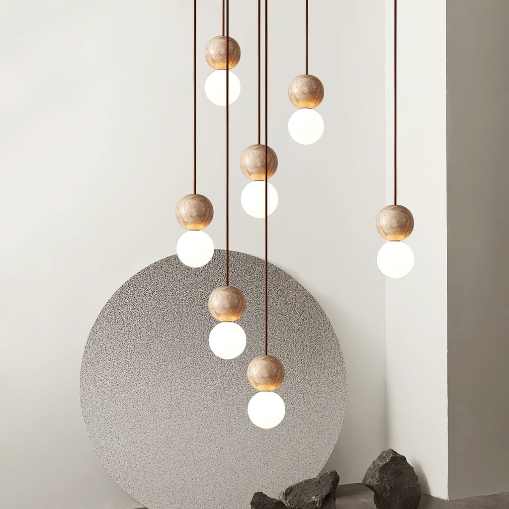 A tall cluster of Clérachic pendants cascades past a round stone panel and rocks, travertine spheres glowing above opal glass globes.
