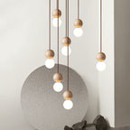 A tall cluster of Clérachic pendants cascades past a round stone panel and rocks, travertine spheres glowing above opal glass globes.