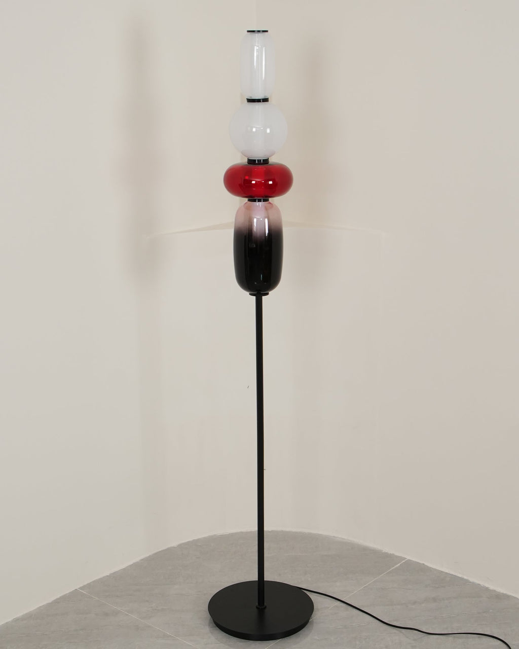 Hand-blown glass floor lamp lit beside a textured wall