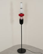 Hand-blown glass floor lamp lit beside a textured wall