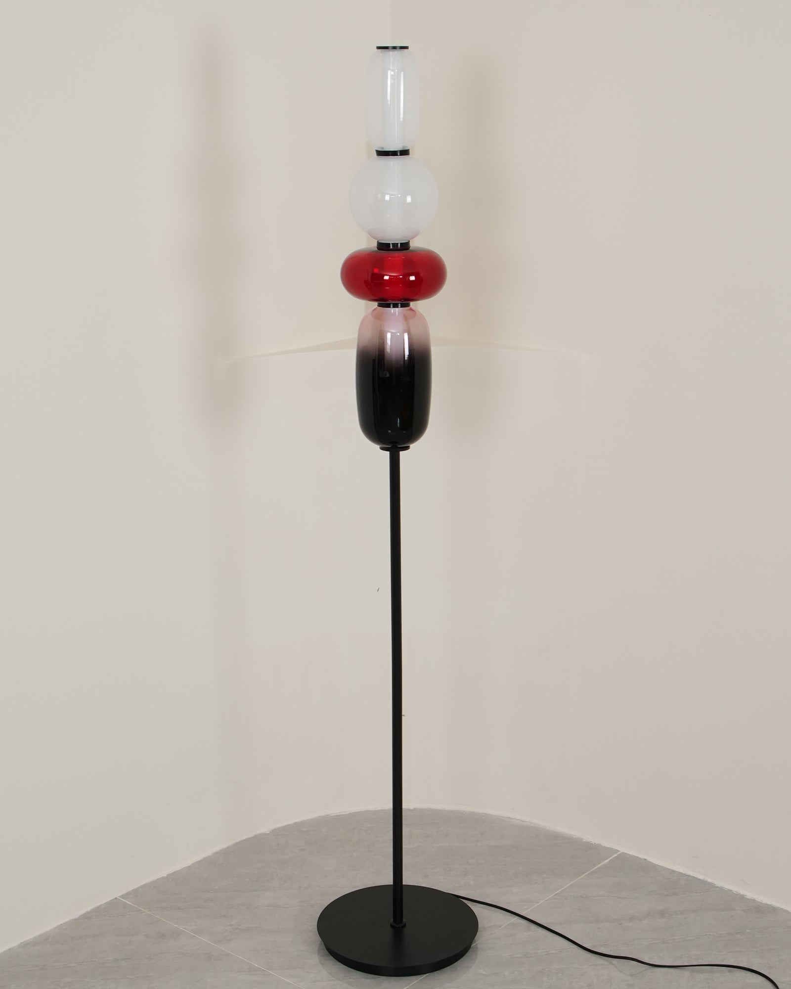 Hand-blown glass floor lamp lit beside a textured wall
