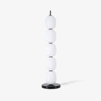 The unlit lamp small against an off-white studio wall, its shadow falling to the right.