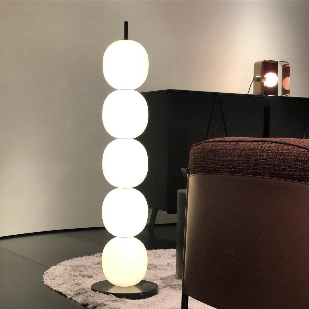 Lit lamp standing on a small white rug beside a black sideboard and a brown leather armchair.