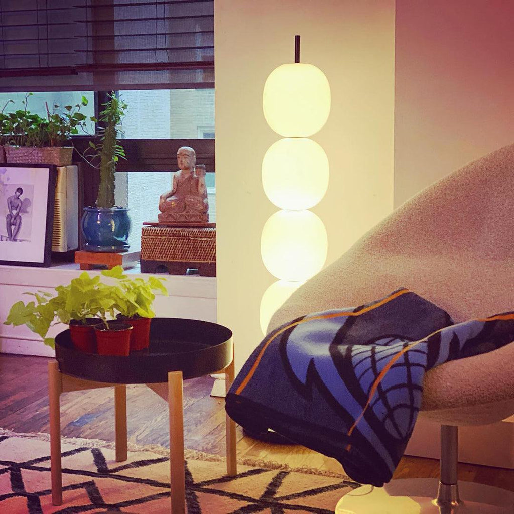 Lit lamp behind a boucle chair draped with a blue blanket, its lower globes hidden.