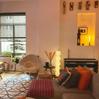 Lit lamp in a loft corner between a black piano and a side table with orange flowers in a vase.