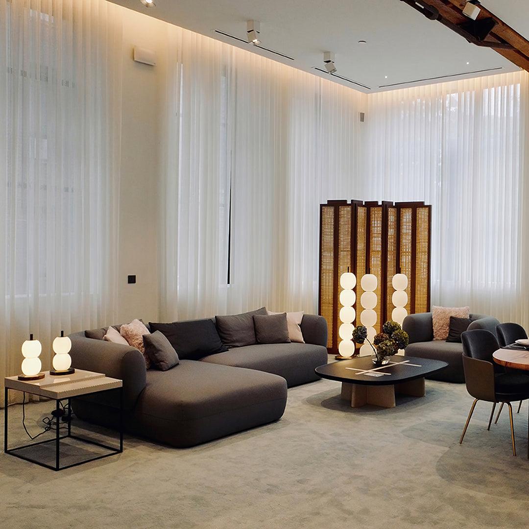 Three lit lamps across a showroom lounge, with two small two-globe versions on a side table.