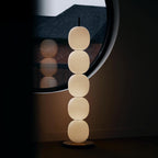 The lit lamp in a dark room beside a round black mirror, its glow repeated in the reflection.