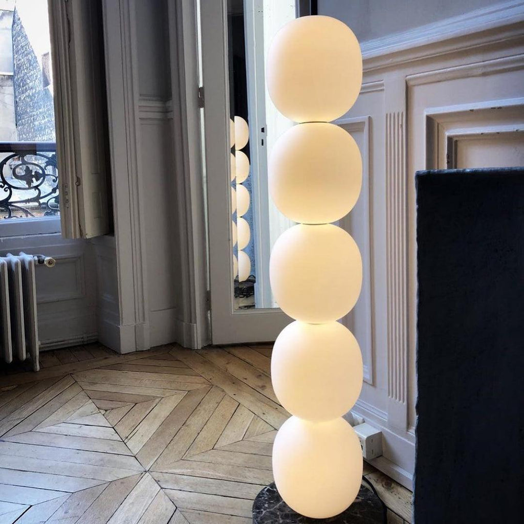 Close view of the lit lamp on star-patterned parquet, all five globes glowing by a balcony door.